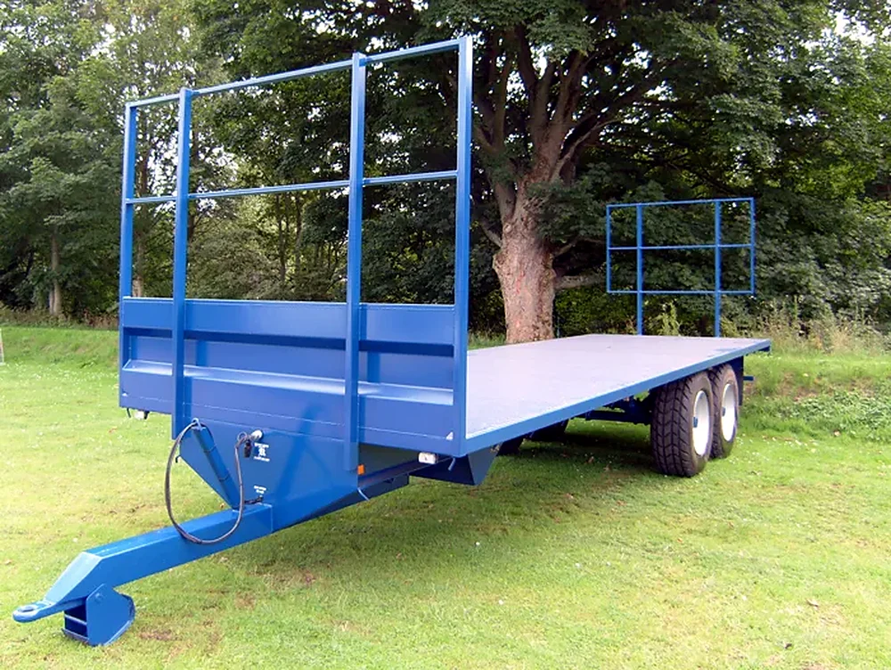 Blue twin axle flat trailer with bale retainer in front of trees